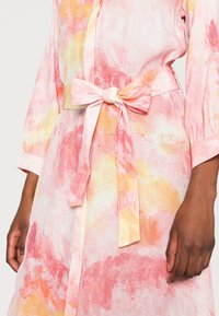 Blumenkleid mit Aquarelltönen in Rosa und Gelb. Es hat eine taillierte Silhouette und eine Schleifendetail; aus leichtem Stoff gefertigt.