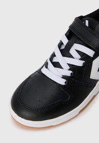 Svart lädersneaker med vita snören, perforerat tåparti och kontrasterande vitt logotyp. Har en gummisula och ankelrem för säker passform.
