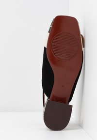 Semelle d'une chaussure à talon haut noire et blanche avec une semelle en cuir marron et un embout de talon texturé, affichant le nom de la marque « Chie Mihara ».
