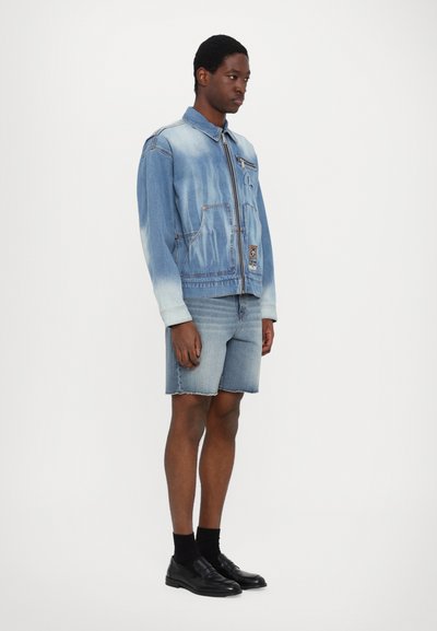 Τζάκετ από τζιν με ανοιχτό gradient, δύο μπροστινές τσέπες και εμβληματική διακόσμηση; συνδυασμένο με τζιν σορτς μέχρι το γόνατο και μαύρες εσπαντρίγιες.