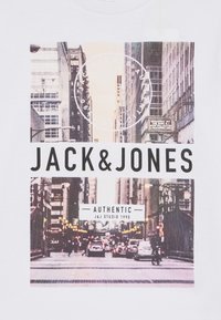 Hvit bomull T-skjorte med grafisk trykk av en urban gate-scene med teksten "JACK&JONES" og "AUTHENTIC" i fete svarte skrifter.