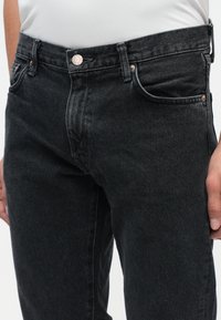 Sorte denim jeans med slim fit, der har en kobberknaplukning, frontlommer og syede detaljer. Tekstureret stof med let falming.