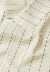 Tissu crème avec de fines rayures verticales noires et un détail de couture pliée créant une texture en couches.