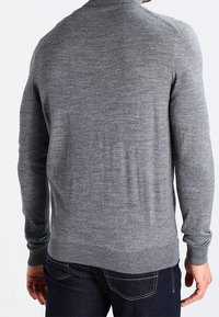 Maglione grigio a maglia con maniche lunghe, scollo rotondo e orlo a coste. La texture appare liscia e aderente, senza motivi o elementi metallica visibili.