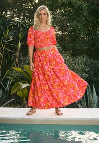 Ensemble deux pièces comprenant un haut smocké à manches courtes et une longue jupe à volants, avec des motifs floraux vifs en rose et orange.