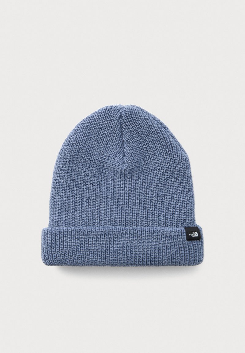 Lyseblå strikket beanie med foldet kant og et lille sort mærke med et hvidt logo på hvid baggrund.