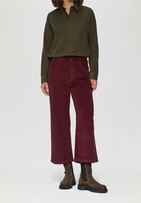 Olijfgroene button-up shirt, gecombineerd met bordeauxrode corduroy wijdvallende broeken. Bruine enkellaarsjes hebben elastische zijpanelen en een chunky zool.