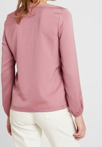 Pitkähihaisen paidan pehmeä ruusupinkki väri, pyöreä kaula-aukko, kevyesti rypytetyt hihansuut ja sileä, kevyt materiaali.