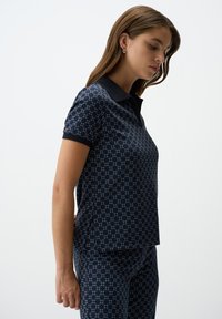 Marine polo shirt met korte mouwen, textuurpatroon van diamanten in lichtere tinten, en een zwarte kraag. Gecombineerd met bijpassende broek.