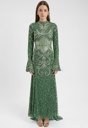 Vestido verde con lentejuelas, de manga larga, con intrincados bordados de cuentas y un corsé ajustado que fluye hacia una falda acampanada. Sandalias doradas complementan el look.