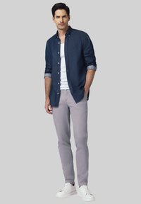 Męski strój składający się z granatowej jeansowej koszuli zapinanej na guziki, białego T-shirtu, jasnoszarych spodni i białych sneakersów. Gładkie tekstury i dopasowany krój.