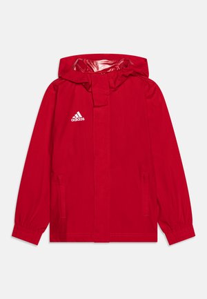 Giacca Adidas rossa con cappuccio, polsini elasticizzati e tasche laterali. Presenta un logo bianco sul lato sinistro del petto e una texture esterna liscia.