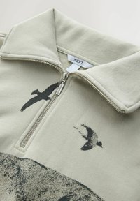 Mikina so štvrťzipom z fleece v svetlozelenej farbe, s čiernym grafickým motívom vtáka a strieborným zipsom. Mäkká textura s konštrukciou goliera.