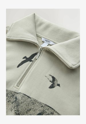 Fleece quarter-zip top in pale green, featuring a black bird graphic and a silver zipper. Soft texture with a structured collar design.