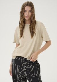 Beige relaxed-fit t-shirt with short sleeves, paired with black patterned trousers featuring abstract white lines and shapes.
