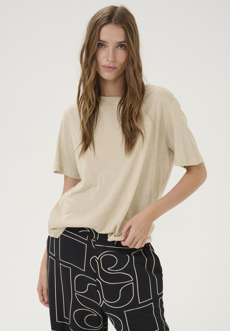 Beige relaxed-fit t-shirt with short sleeves, paired with black patterned trousers featuring abstract white lines and shapes.