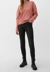 Rosa stickad tröja med rund halsringning, tillsammans med svarta läderbyxor. Outfiten kompletteras med svarta snörade kängor.