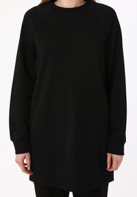 Sudadera negra de corte relajado, con cuello y puños de canalé. Confeccionada en una tela suave, presenta un bajo trasero ligeramente más largo.