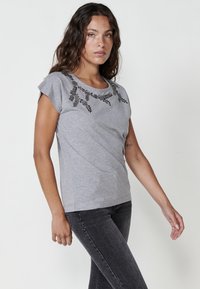 Grå kortärmad t-shirt med dekorerad blommönster vid halslinjen, tillverkad av mjukt tyg med en figurnära passform.