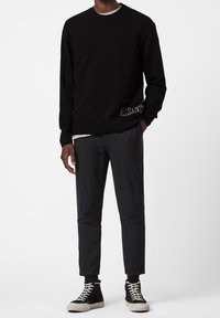 Czarny dziergany sweter z okrągłym dekoltem, z bocznym detalem z logo. W zestawie z ciemnymi spodniami i czarnymi wysokimi trampkami.