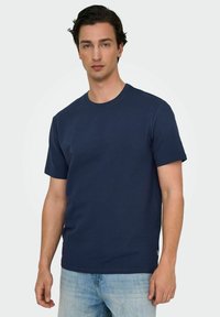 Marineblå kortærmet t-shirt med en tekstureret, ribbet design. Rund halsudskæring og lige kant, parret med lyseblå denim jeans.