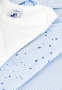 Tre capi d'abbigliamento per neonati: un body bianco in cotone, una camicia azzurra con stampe di stelle e una maglietta a righe blu, tutti con texture morbide.