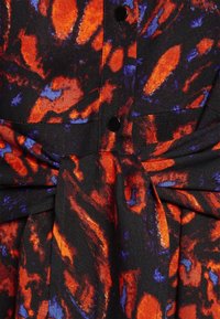 Zwarte stof met een wirrend abstract patroon in levendig rood en blauw, met knopen en een tailleontwerp met plooien. Getextureerde afwerking.