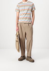 Gestreiftes Baumwoll-T-Shirt in Beige, Blau, Orange und Grün; lockere hellbraune Hose; beigefarbene Tasche; braune strukturierte Stiefel mit dicken Sohlen.