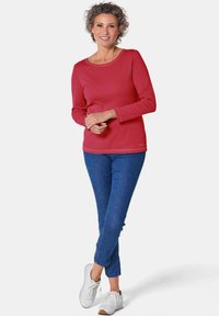 Rode langarmshirt met een ronde hals, gecombineerd met blauwe jeans en witte sneakers. Het shirt heeft eenvoudige stikdetails.