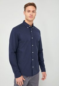 Marineblauwe knoop-shirt gemaakt van katoen, voorzien van een borstzak, lange mouwen en witte knopen aan de voorkant. Soepele textuur.