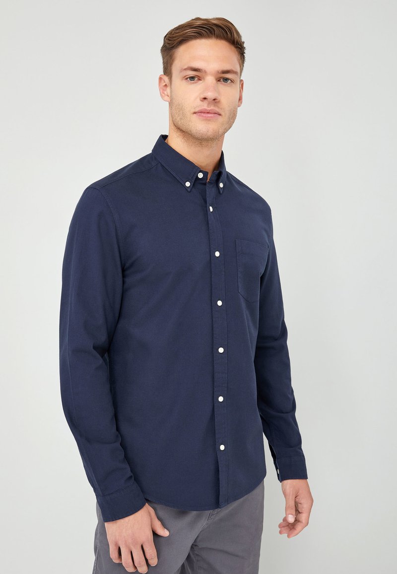 Marineblauwe knoop-shirt gemaakt van katoen, voorzien van een borstzak, lange mouwen en witte knopen aan de voorkant. Soepele textuur.