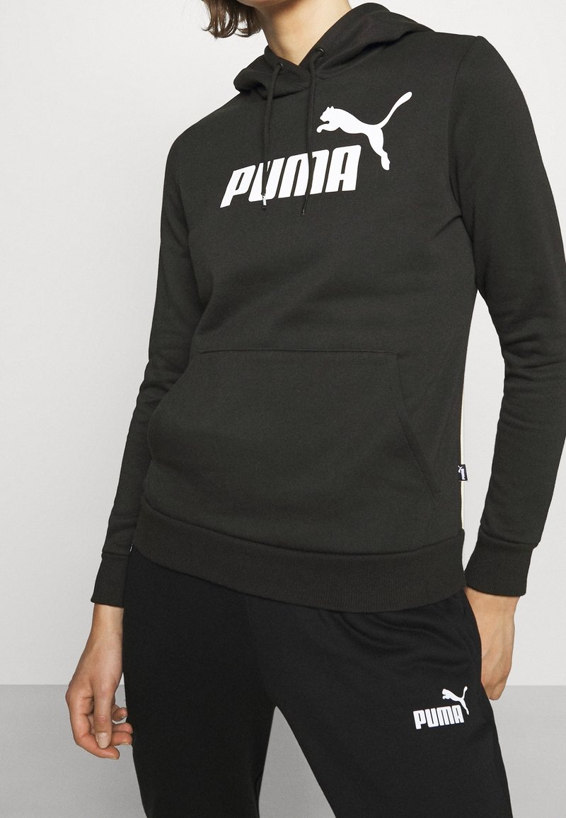 Felpa con cappuccio nera realizzata in morbido tessuto, con un grande logo Puma bianco sul petto e una tasca frontale. Design semplice, silhouette aderente.