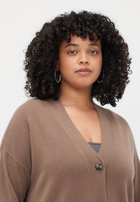 Brown, knitted cardigan with a V-neckline, single button closure, and drop shoulders. Features a soft texture and slightly oversized fit.