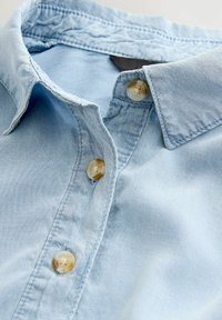 Chemise en denim bleu clair avec col pointu, cinq boutons avec une finition translucide et de subtils détails de couture.