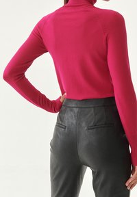 Dopasowany sweter z golfem w jaskrawym różowym kolorze, wykonany z miękkiego materiału, zestawiony z wysokim stanem czarnych skórzanych spodni z tylnymi kieszeniami.