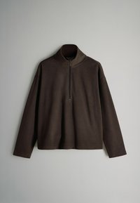 Hnedý fleecový pulóver s vysokým golierom a polovičným zipsom. Má spadnuté ramená a dlhé rukávy. Mäkká textúra a voľný strih.