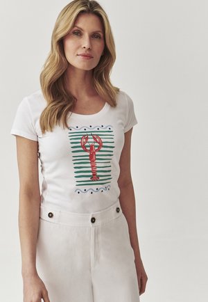 Hvid t-shirt med et rødt hummer grafik og grøn stribet baggrund, med scoop-neck og korte ærmer, parret med cremede bukser.