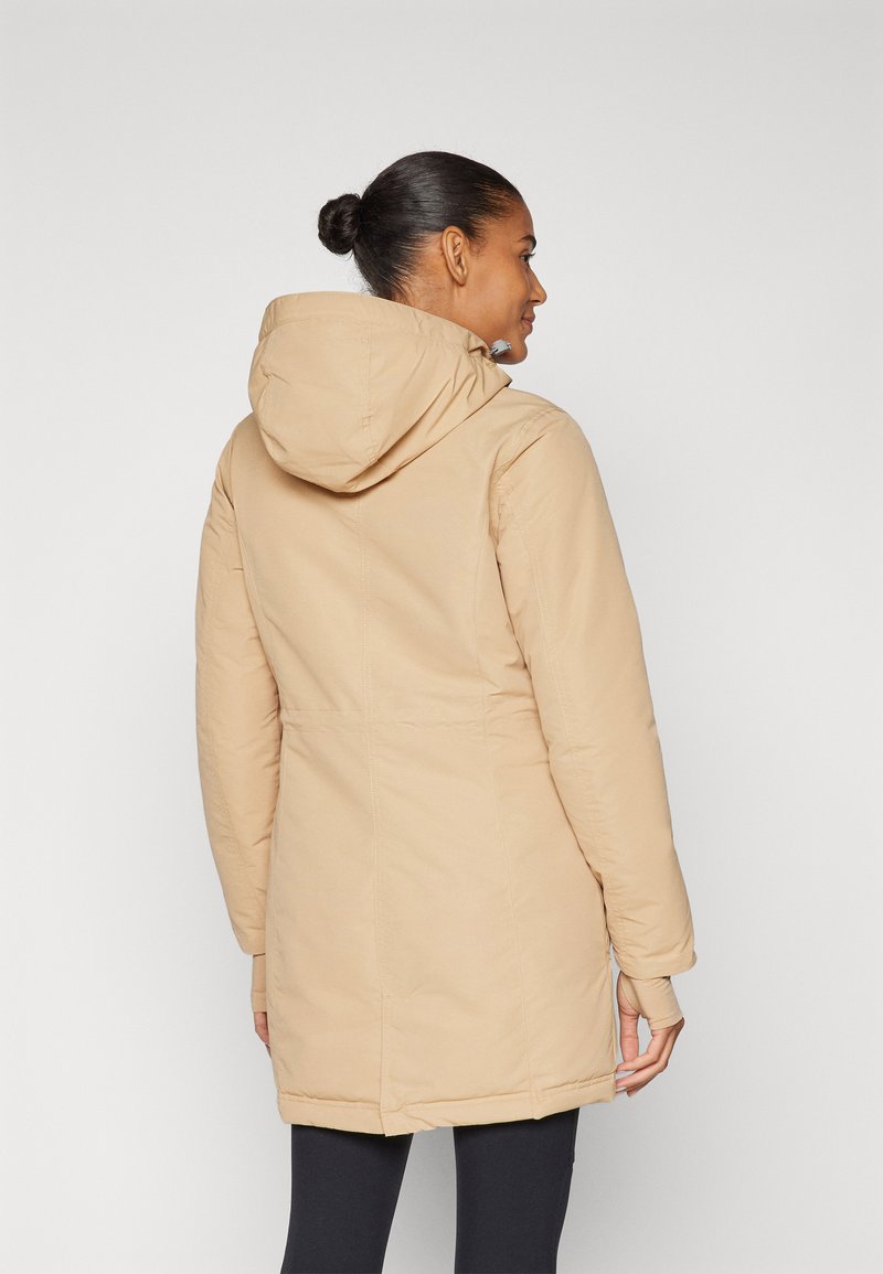 Manteau doudoune beige clair à capuche avec une taille cintrée, des manches longues et une texture lisse ; présente un dos plus long et des détails de couture cachés.