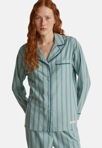 Světle modrý pruhovaný pyžamový set vyrobený z měkké látky, obsahující košili na knoflíky s kapsou na hrudi a odpovídající kalhoty s elastickým pasem.