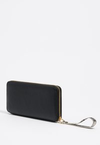 Cartera de cuero negro con acabado texturizado, cierre con cremallera dorada y una correa decorativa para la muñeca que presenta un acento impreso.