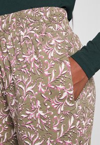 Calças de tecido com padrão floral em verde-azeitona com detalhes em rosa e branco. Apresentam uma cintura elástica e bolsos laterais.