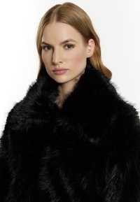 Sort faux fur sjal med en bred krave, der har en blød, tekstureret finish og et struktureret design omkring udskæringen.