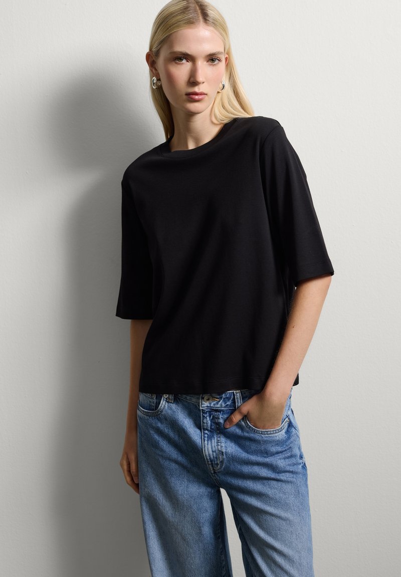 Zwarte, korte mouwen shirt van zachte stof, met een ronde halslijn en een relaxte pasvorm, gecombineerd met lichtblauwe, losse spijkerbroek.