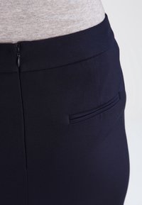 Jupe bleu foncé à texture lisse, avec une poche arrière et une fermeture éclair dissimulée à la taille pour une silhouette ajustée.