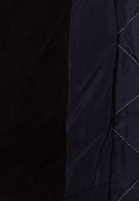 Tissu noir et marine présentant un côté en tissu matelassé lisse et brillant et un autre côté à texture douce et duveteuse, avec des surpiqûres contrastantes.