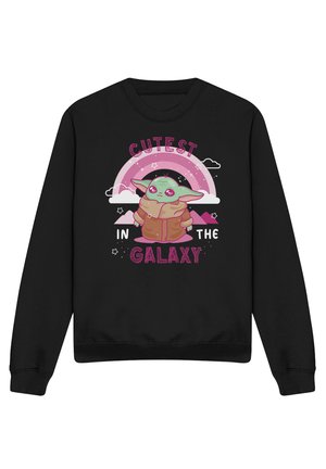 Schwarzer Pullover mit einer grünen Cartoon-Figur in einem braunen Mantel unter einem pinken Regenbogen und dem Text „Süßester in der Galaxie."