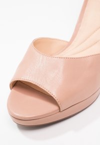 Escarpin à bout ouvert en cuir rose pâle. Présente une texture lisse et une ouverture ronde et large. Comprend une semelle compensée basse et un détail de couture subtil.