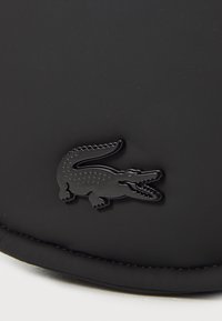 Svart vanntett bøttehatt laget av glatt materiale, med en teksturert svart krokodille-logo på forsiden. Enkel, funksjonell design.