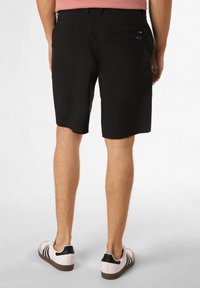 Zwarte shorts met een rechte voorkant, een achterzak met ritssluiting en een gladde textuur. Gecombineerd met witte sneakers met zwarte strepen.
