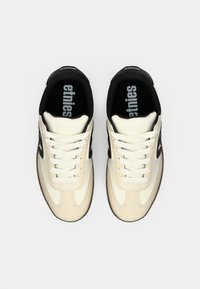 Sapatos Etnies com um upper bege, detalhes em preto e atacadores brancos. Apresenta uma superfície texturizada e palmilhas acolchoadas pretas com a marca.